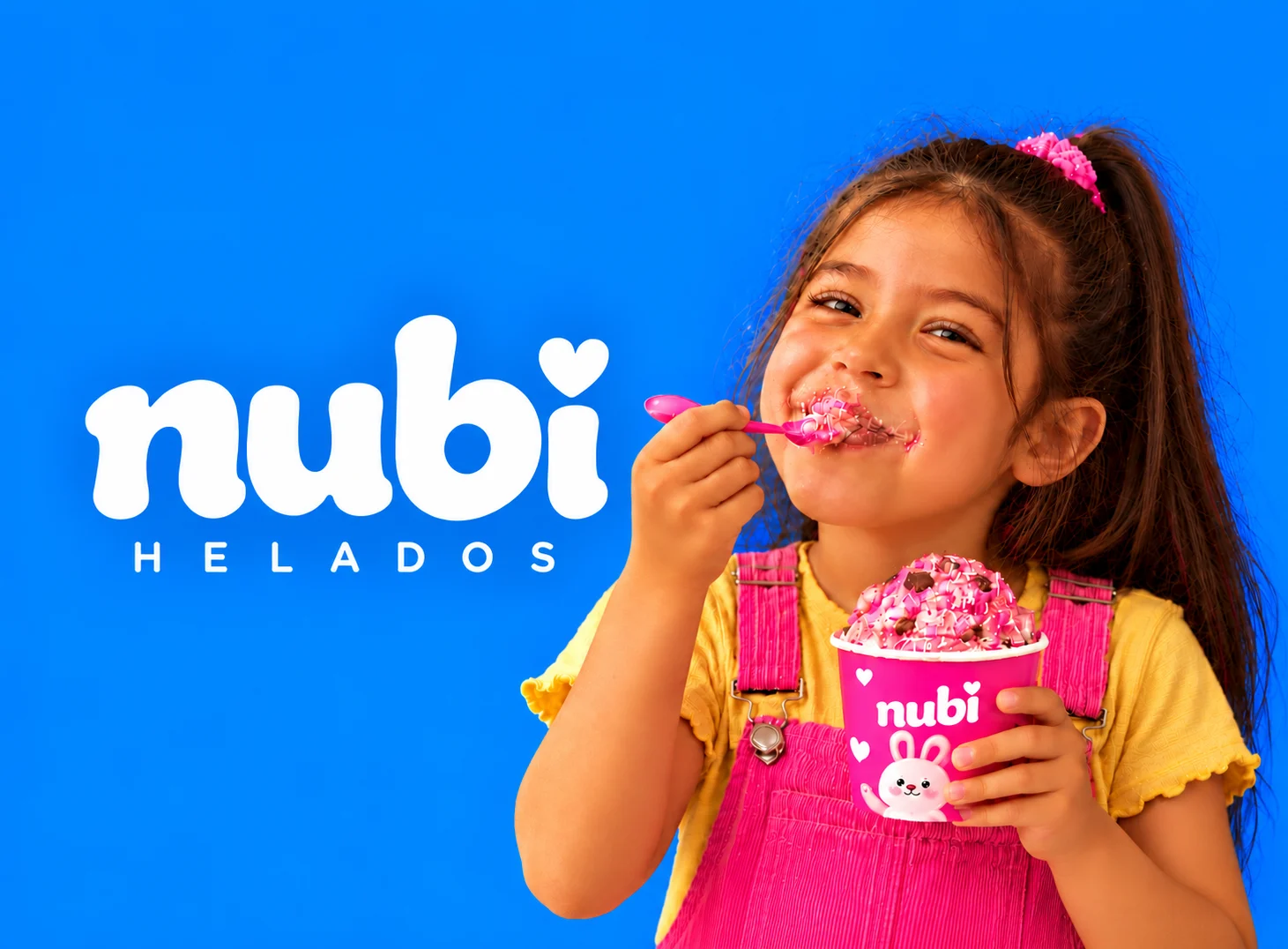 Nubi: niña sonriente comiendo un helado rosa de la tarrina Nubi junto al logotipo, sobre fondo azul